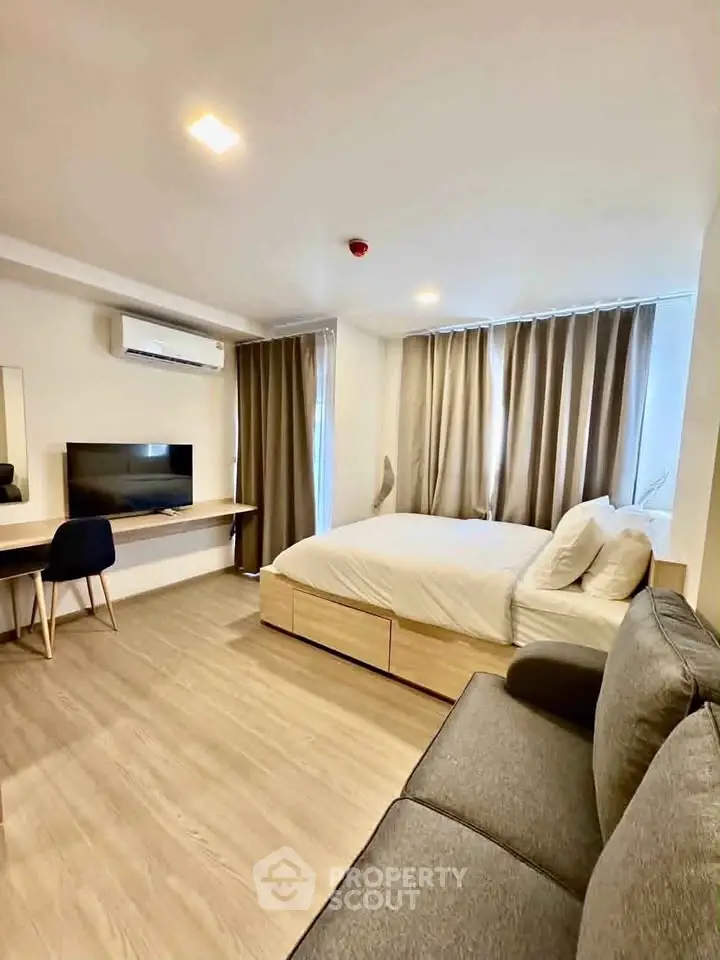 Modern studio apartment with cozy bed, sofa, and workspace, featuring sleek design and ample natural light.