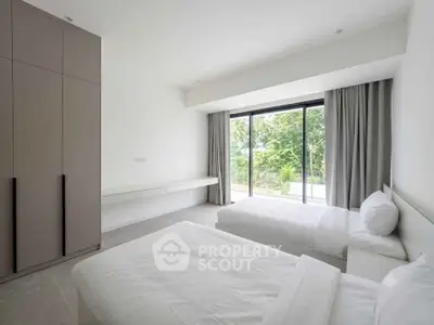 Spacious bedroom with twin beds and large window offering lush garden view.