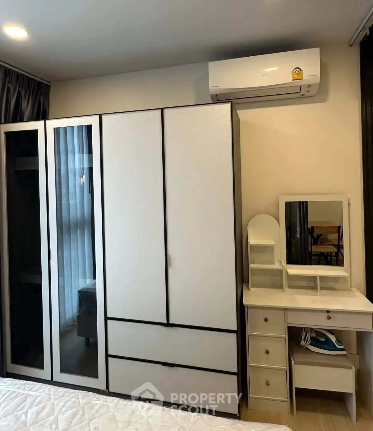 Modern bedroom with sleek wardrobe and vanity set under air conditioning unit.