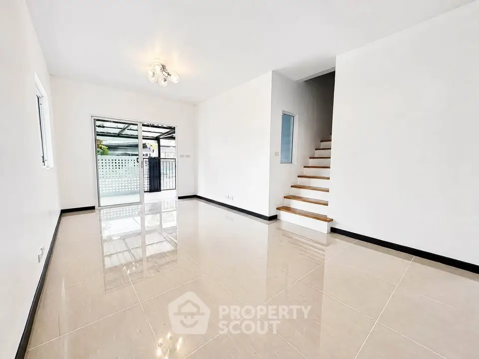 Spacious modern living room with glossy tiled floors and staircase leading to upper level.