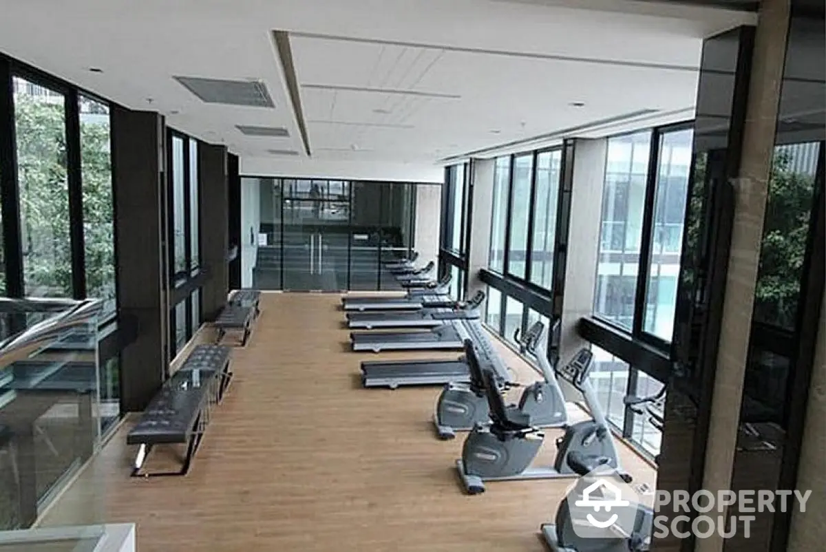 Modern gym with large windows and state-of-the-art equipment in luxury residential building.