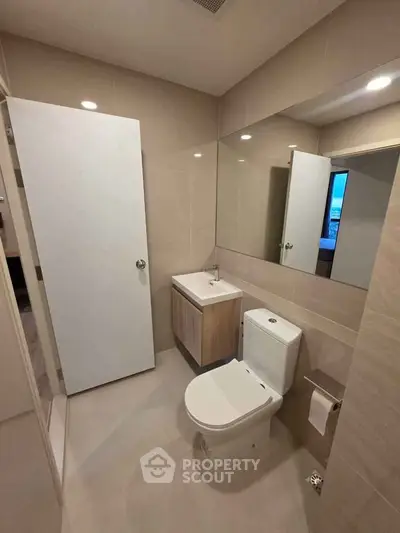 Modern bathroom with sleek fixtures and neutral tones, featuring a compact vanity and large mirror.