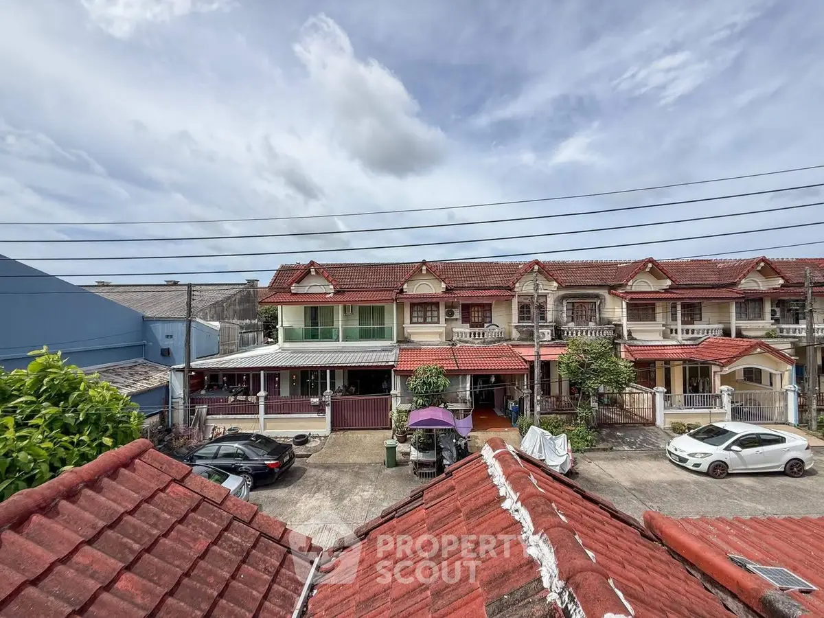 Charming residential neighborhood with red-roofed townhouses and parked cars under a cloudy sky.