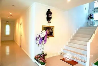 Elegant entryway with pristine white staircase, adorned with decorative flowers and classic wall clock, leading to a welcoming, bright interior.