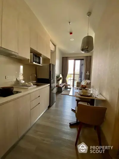 Modern kitchen with sleek cabinetry and integrated appliances flows into a cozy dining area, leading to a sunlit balcony with inviting views.