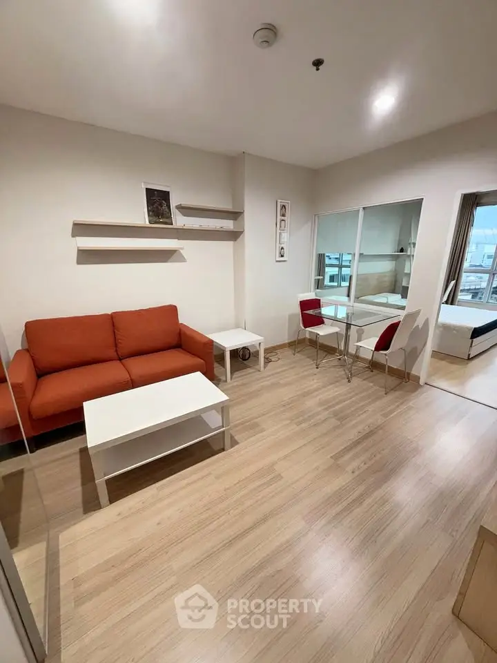Modern living room with red sofa, wooden flooring, and glass dining table in cozy apartment.
