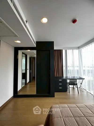 Modern bedroom with large windows and a study desk, featuring sleek wooden flooring and contemporary design.