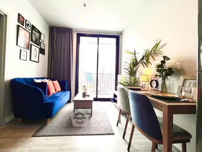Stylish living room with blue sofa and dining area, featuring large window and modern decor.