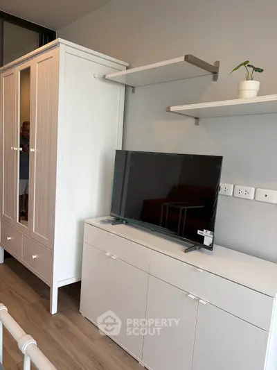 Modern living room with sleek TV stand, wall-mounted shelves, and stylish wardrobe in a cozy apartment.