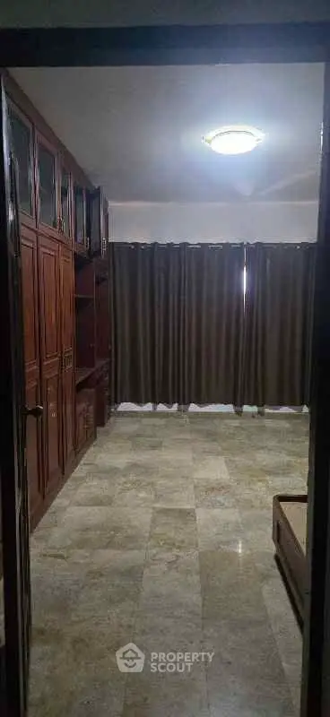 Spacious bedroom with elegant wooden cabinetry and large window with curtains.