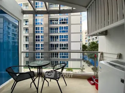 Modern balcony with glass railing and outdoor seating overlooking contemporary apartment complex.