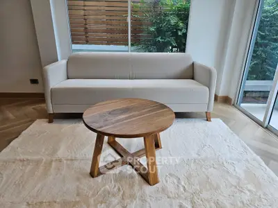 Modern living room with elegant white sofa and wooden coffee table, featuring large windows and natural light.