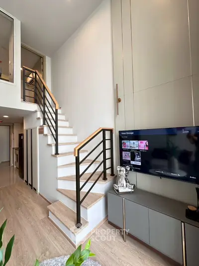 Modern living room with stylish staircase and wall-mounted TV in elegant home interior.