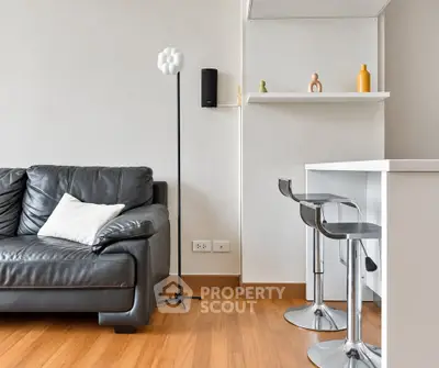 Modern living room with sleek black leather sofa and stylish bar stools in a contemporary apartment.