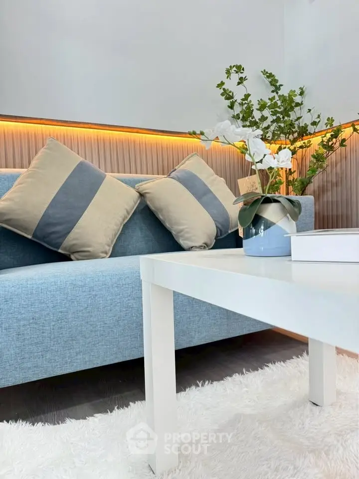 Stylish living room with modern blue sofa, decorative pillows, and elegant white coffee table on plush rug.