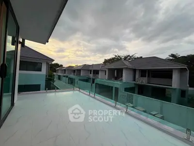 Luxurious modern balcony with glass railing offering stunning views of contemporary villas at sunset.