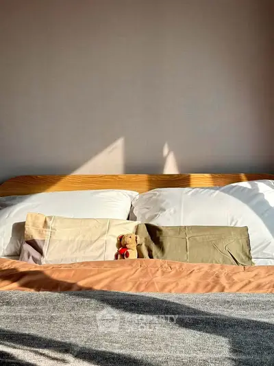 Cozy bedroom with sunlight streaming onto a neatly made bed and decorative pillows.