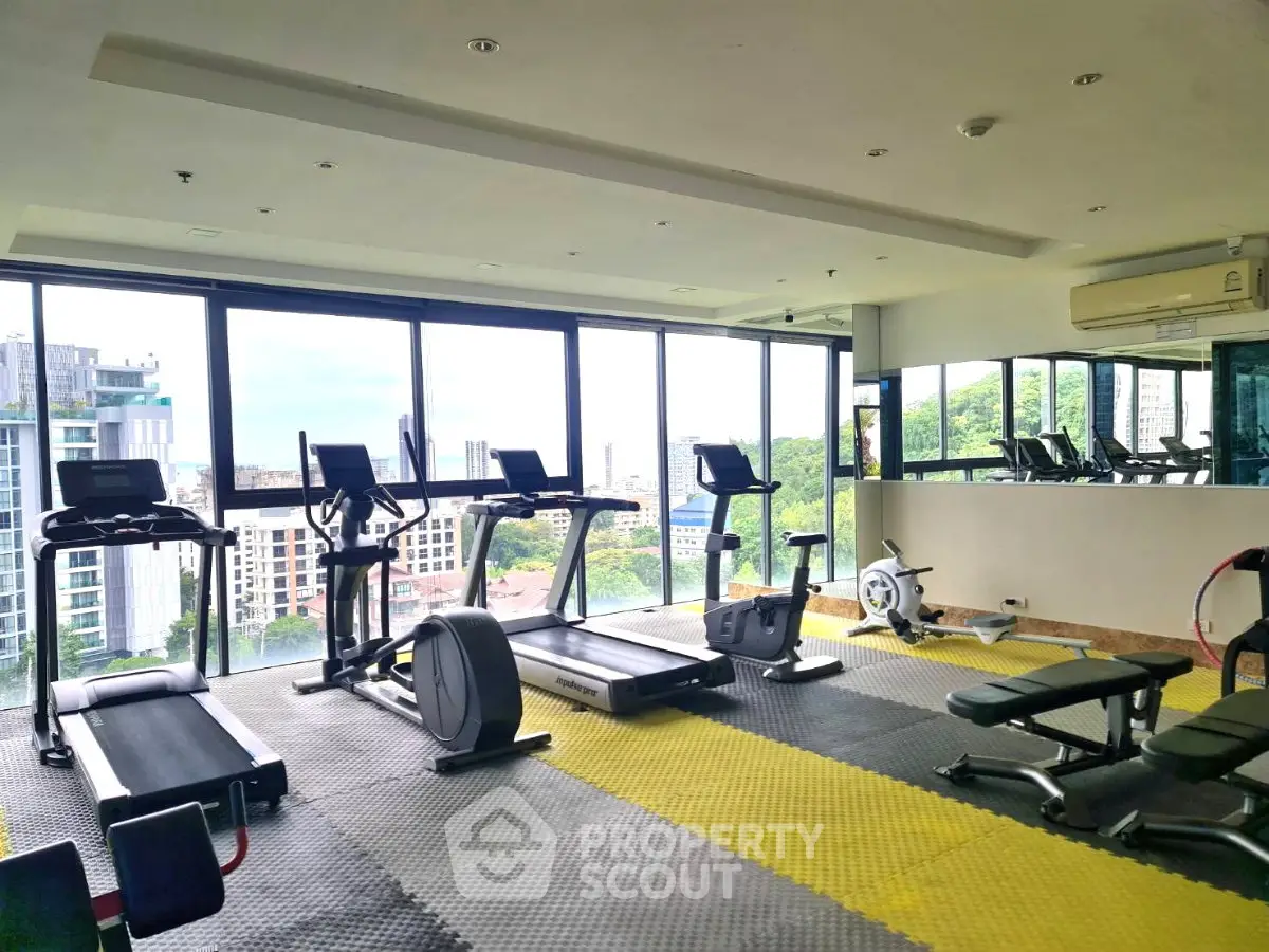Spacious gym with modern equipment and panoramic city views in luxury apartment building.