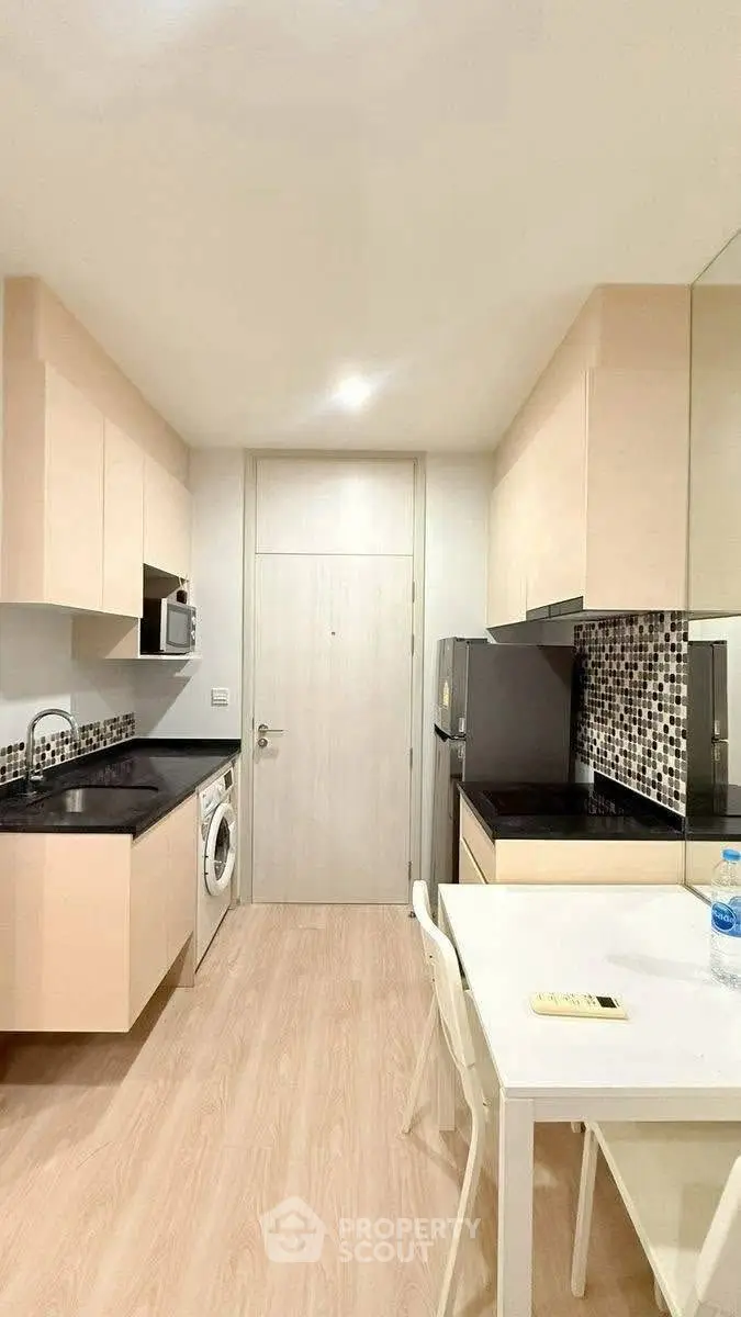 Modern kitchen with sleek cabinets, washing machine, and dining area in stylish apartment.