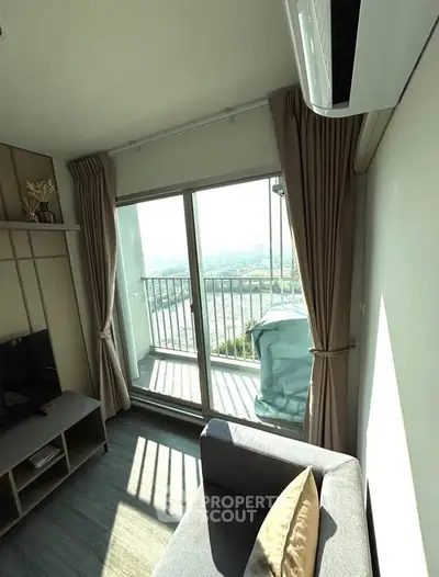 Bright living room with large window and balcony access, featuring modern decor and air conditioning.