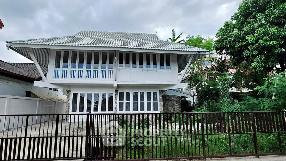 Charming two-story house with unique architectural design and lush greenery, perfect for serene living.