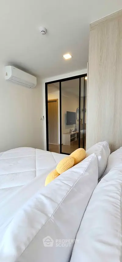 Modern bedroom with cozy bedding and air conditioning, featuring a sleek glass partition.