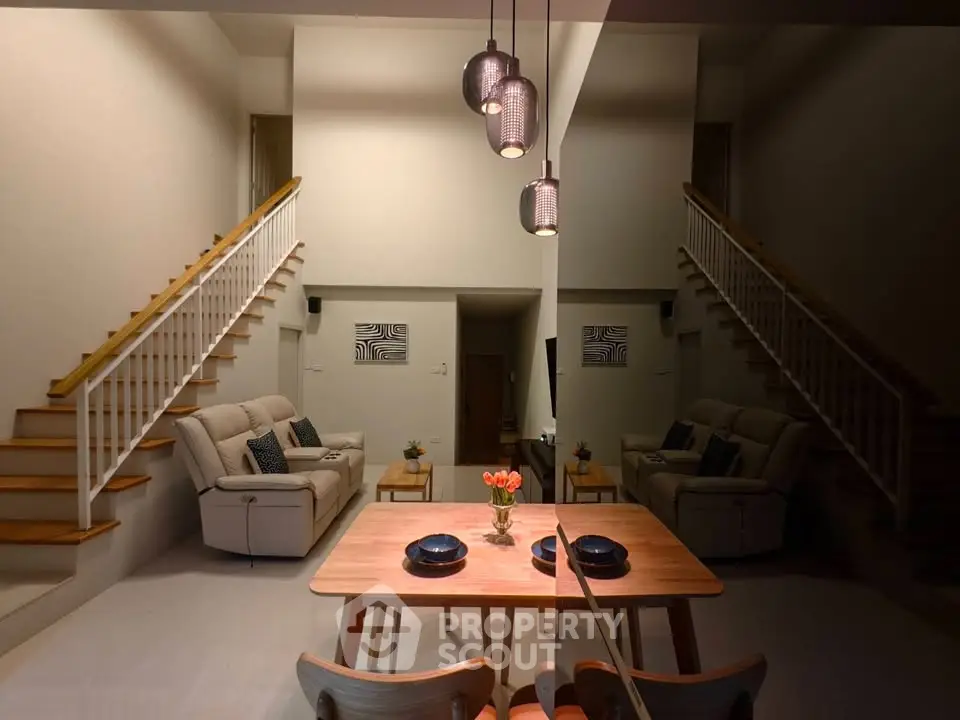 Elegant living room with high ceiling and modern decor, featuring a stylish dining area and dual staircases.