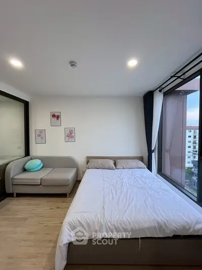 Modern bedroom with large window and cozy seating area in a stylish apartment.