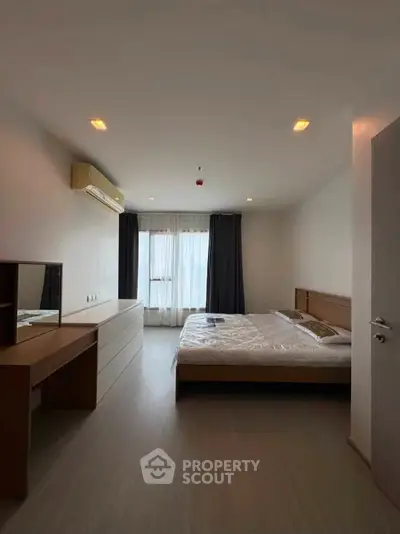 Spacious bedroom with modern furnishings and natural light from large window.