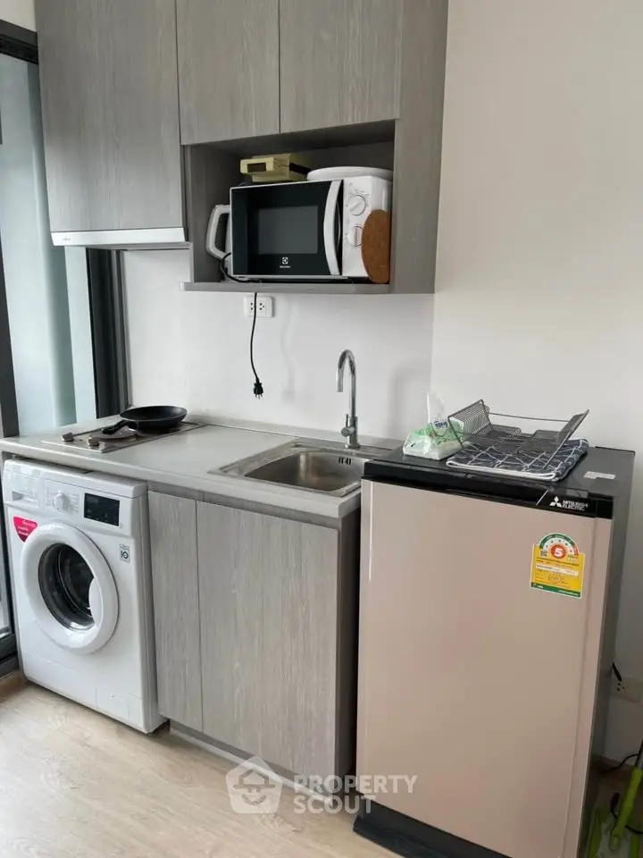 Modern compact kitchen with washing machine and microwave in sleek apartment.