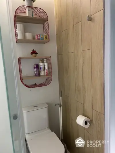 Compact modern bathroom with wall-mounted shelves, wooden door, and white ceramic fixtures for space-efficient urban living.