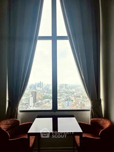 Stunning city view from a high-rise apartment window with elegant curtains and cozy seating area.
