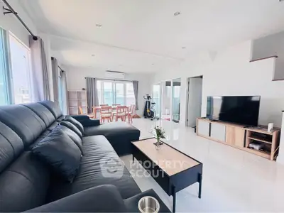 Spacious modern living room with sleek black sofa and large TV, perfect for relaxation.