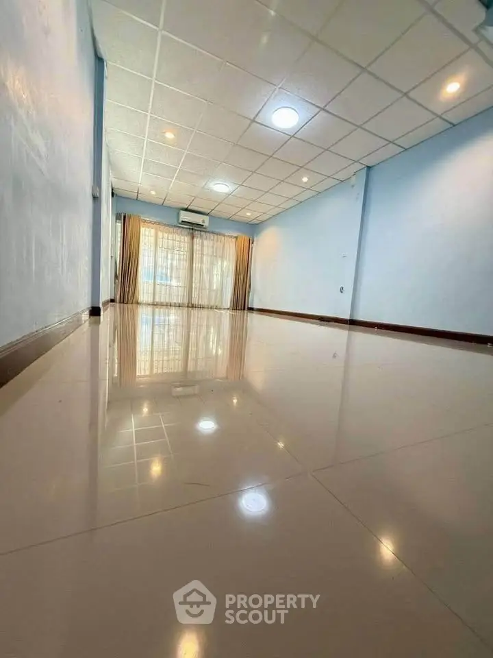 Spacious empty room with glossy tiled floor and large window, perfect for customization.