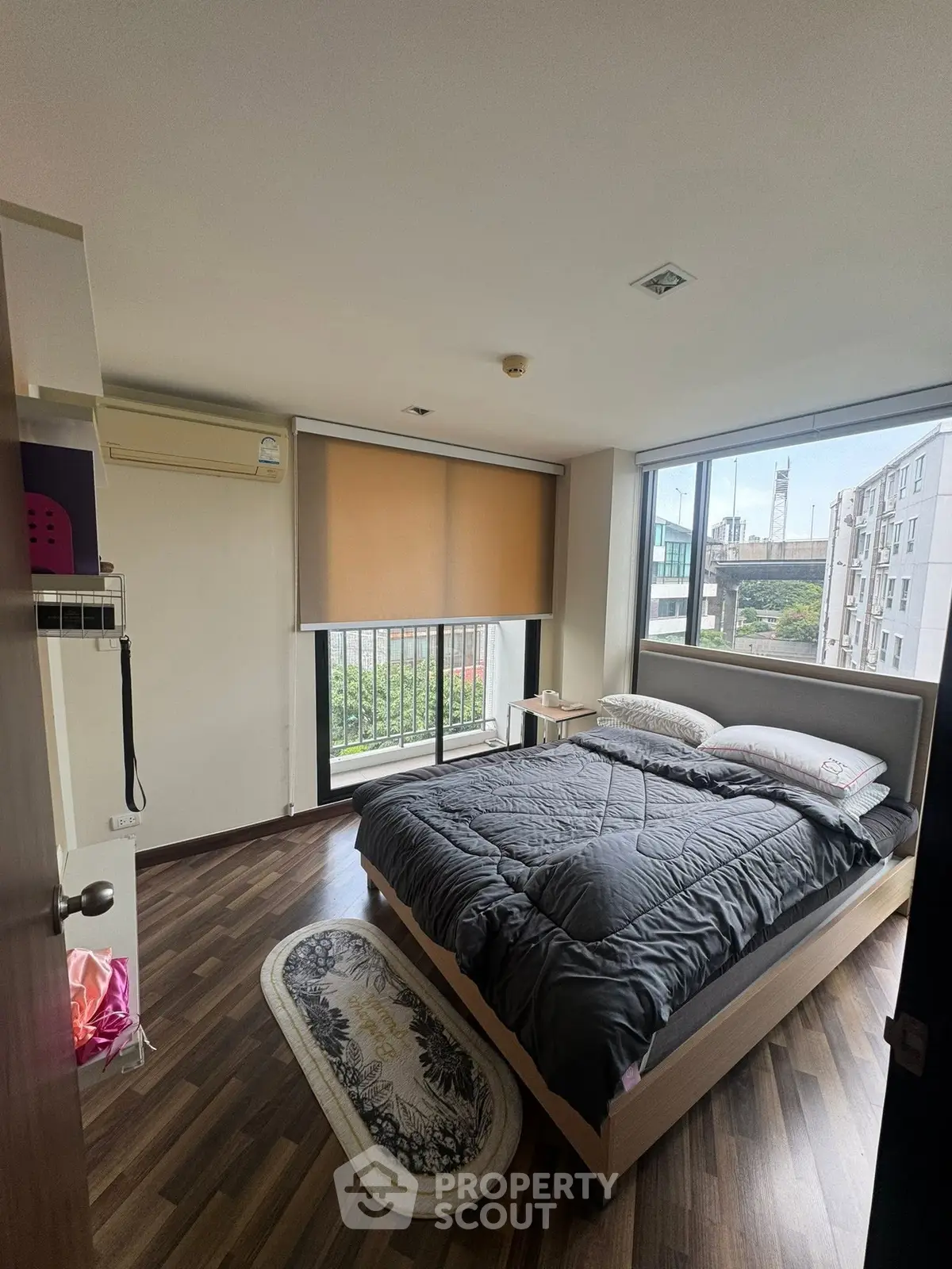 Modern bedroom with large windows and city view, featuring stylish decor and natural light.