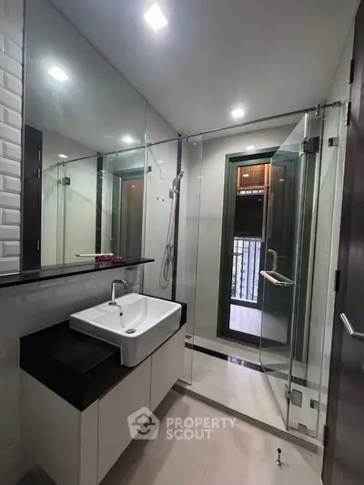 Modern bathroom with glass shower and sleek vanity in contemporary apartment.