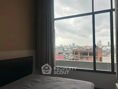 Cozy bedroom with large window offering stunning cityscape views, perfect for urban living.