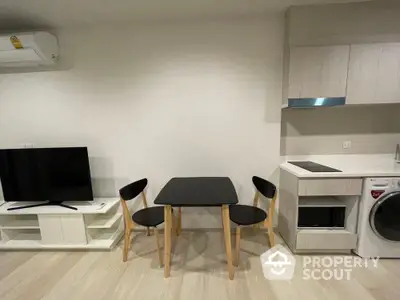 Modern compact living area with dining set, TV, and kitchenette featuring washing machine and microwave.