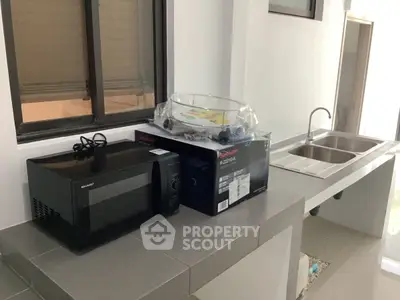 Modern kitchen with microwave and double sink, featuring sleek countertops and ample natural light.