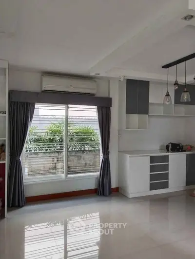 Spacious modern living room with large window and sleek kitchen area, perfect for contemporary living.