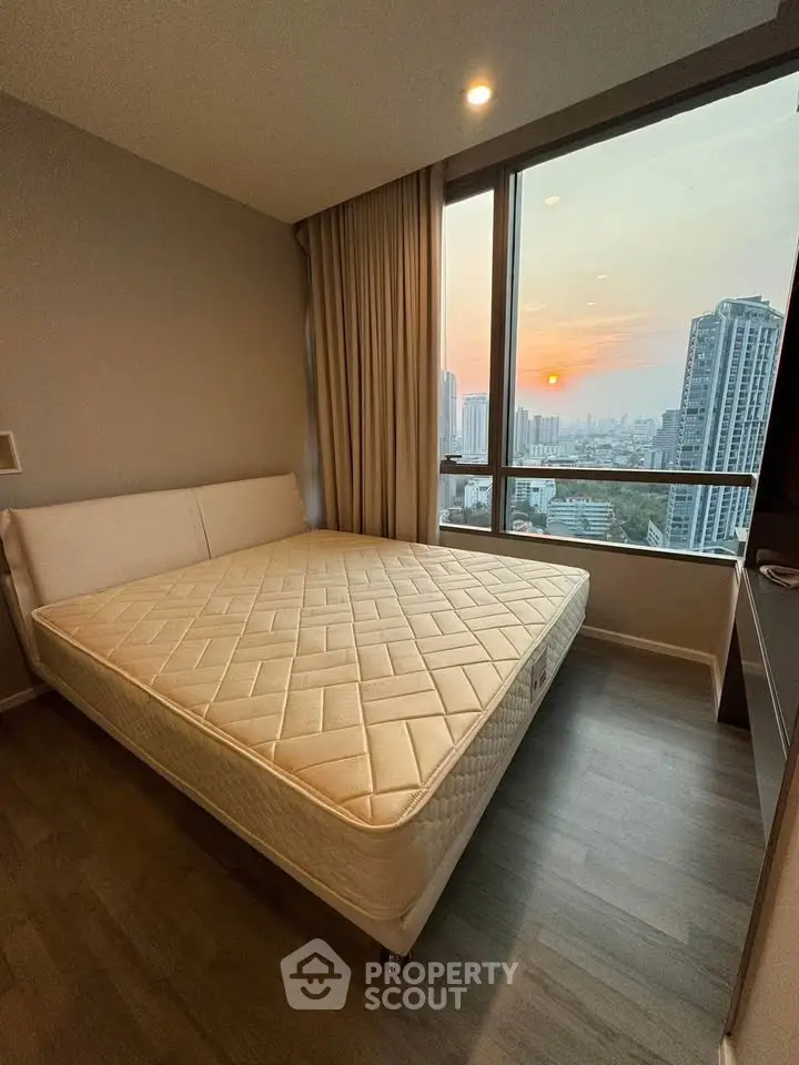 Modern bedroom with large window offering stunning city view at sunset.
