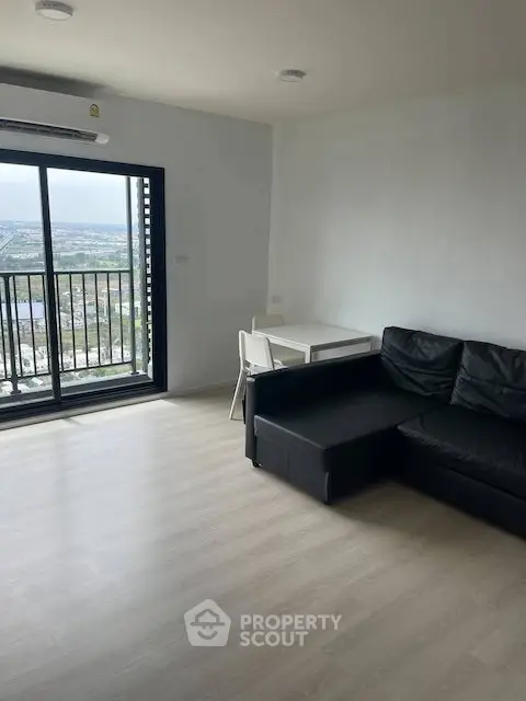 Modern living room with balcony and city view, featuring sleek black sofa and dining area.