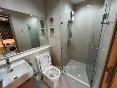 Modern bathroom with glass shower and washing machine in sleek apartment.