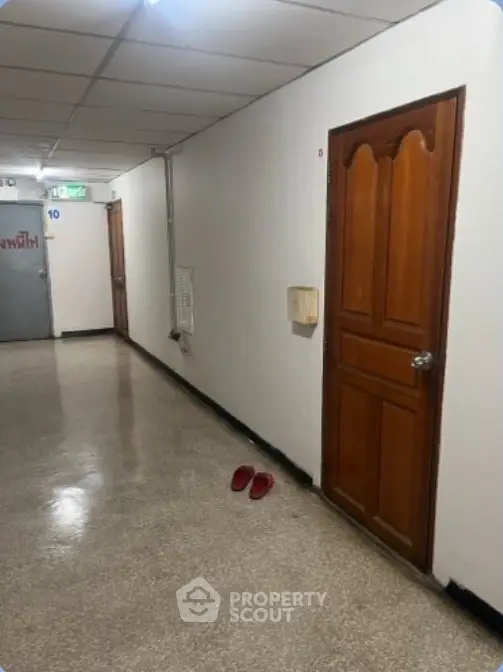 Apartment hallway with wooden doors and slippers on the floor, showcasing a simple residential corridor.