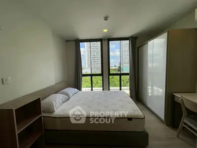 Modern bedroom with large window and city view, featuring a comfortable bed and sleek furniture.