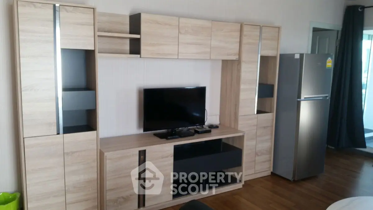 Modern living room with sleek wooden entertainment center and stainless steel fridge.