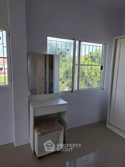 Bright bedroom with large windows and a vanity table, offering a serene view of lush greenery.