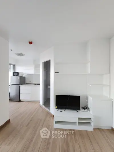 Modern apartment interior with sleek white shelves and compact kitchen area, featuring a small TV setup.