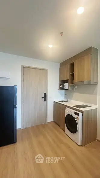 Modern kitchen with wooden cabinets, washing machine, and fridge in a compact layout.
