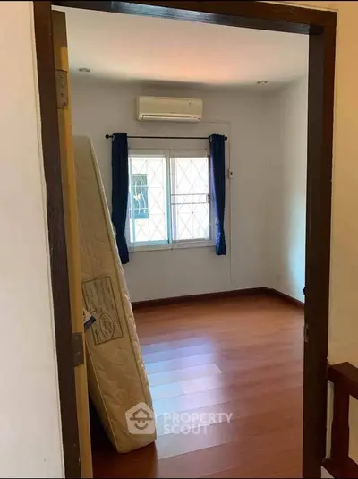 Spacious empty bedroom with wooden flooring and air conditioning.